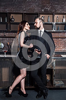 Flirt on a party. Girl holding glasses of vine and looking with passion on bearded man