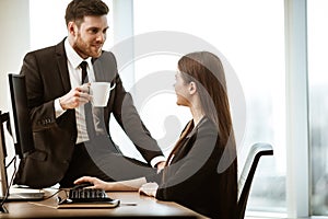 Flirt and relations at work. Smiling male businessman sits and shows sexual interest to positive minded female assistant