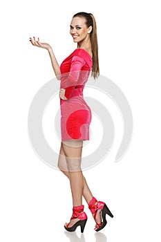 Flirtatious young woman in pink dress showing blank copy space