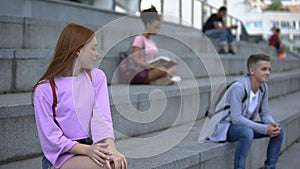 Flirting attractive teen female looking at handsome male student sitting stairs