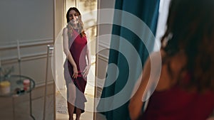 Flirting girl looking mirror in stylish red dress. Smiling model getting ready