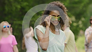 Flirty girl with curly hair dancing, smiling to camera. Friends partying in park