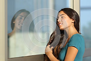 Flirty teen girl combing her hair using a window like a mirror