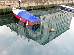 Floating boat and its reflection in the water canal - connection between liquid and solid state, Trieste, Italy