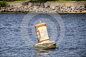 Floating bouy in lake saying Keep Right bobbing on rough water with relfection and blurred shore and rip rap in distance