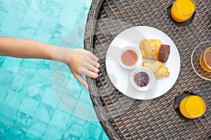 Floating Breakfast tray in swimming pool at luxury hotel or tropical resort villa, desserts; croissant, chocolate roll, pie and