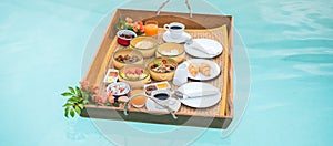 Floating Breakfast tray in swimming pool at luxury hotel or tropical resort villa, fruits, croissant, coffee, and orange juice.