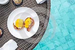 Floating Breakfast tray in swimming pool at luxury hotel or tropical resort villa; poached egg with streaky smoked bacon,