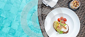 Floating Breakfast tray in swimming pool at luxury hotel or tropical resort villa; smoked salmon with avocado, roasted tomato,