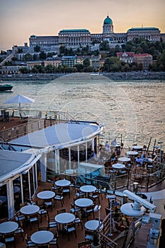 Floating cafes along the promenade and historic building. Evening on the Danube River in Budapest