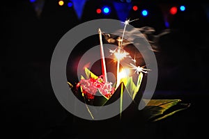 Floating flowers in banana leaves with light on top of candle, joss sticks, and fire works in full moon night