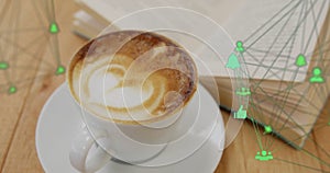 Floating green network icons connecting over white cup with latte art on table beside open book