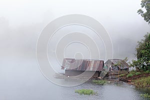 Floating raft house on river with foggy background.