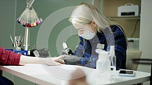 Floating slow motion close up of a young blonde worker in a surgical mask doing a manicure in a beauty salon