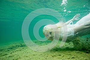 A floating woman. Underwater portrait. Girl in white dress swimming in the lake. Green marine plants, water