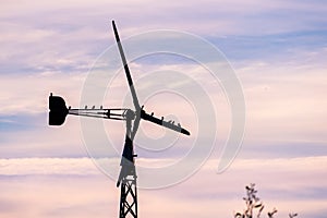 A flock of birds sitting on an old water pumping windmill; sunset sky background; California