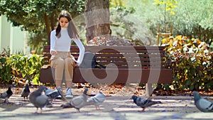 A flock of pigeons on the street near people. Urban birds nourished people. The woman on the bench in the city Park. Girl feeding