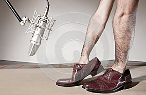 Floey record sound studio. Man hands inside male dress shoes front a professional microphone and over a wood table. FC