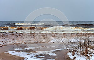 Flood under thin ice in front of big waves of winter sea