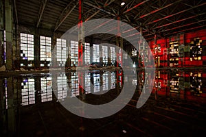 Flooded abandoned large industrial hall illuminated by red lights. Reflection in water. Abandoned Voronezh excavator plant