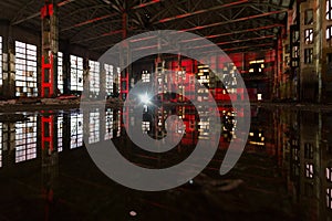 Flooded abandoned large industrial hall illuminated by red lights. Reflection in water. Abandoned Voronezh excavator plant