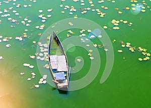 Flooded boat in the green water of a river with leaves of water lilies. Sunny beams