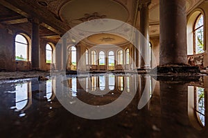 Flooded large hall with columns in old abandoned mansion, water reflection