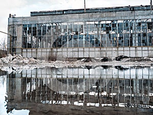 Flooded  territory of abandoned ruined industrial factory building with broken facade and windows, reflection in water