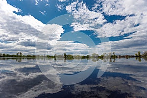 The flooding river in spring on the landscape with blue sky reflection