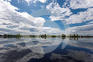 The flooding river in spring on the landscape with blue sky reflection