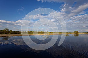 The flooding river in spring on the landscape with blue sky and water