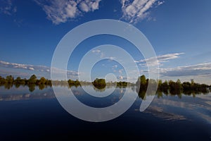 The flooding river in spring on the landscape with blue sky and water