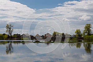 The flooding river in spring on the landscape with blue sky and water and the village