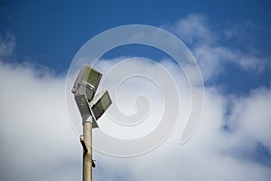 Floodlights above a football pitch with blue sky and clouds in the background