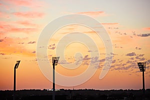 Floodlights silhouetted against an orange, sunset sky.