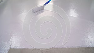 floor painting. dirty repairs and alterations. A worker paints the floor white with a roller. The concrete floor is