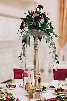 Floral arrangement in red-green tones in a high vase or a golden candlestick
