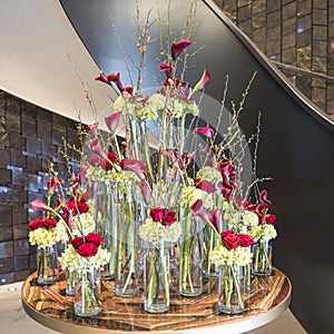 Floral arrangement with red roses, twigs of flowering quince, callas in different glass vases