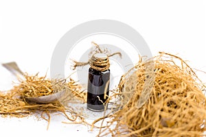 Floral and ayruvedic essence of dried vetiver grass or khus isolated on white in a small transparent glass bottlw with raw khus. photo