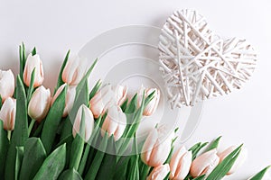 Floral border from bouquet of pink tulips and wooden heart on white background. Anniversary celebration concept. Top view