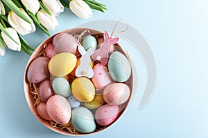 Floral border from bouquet of white tulips, Easter eggs and toys on blue background. Easter celebration concept. Copy space. Top
