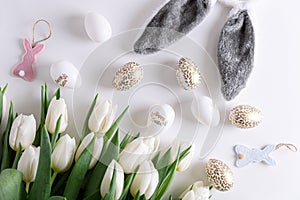 Floral border from bouquet of white tulips, Easter eggs and toys on white background. Easter celebration concept. Copy space. Top