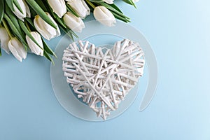 Floral border from bouquet of white tulips and wooden heart on blue background. Anniversary celebration concept. Top view