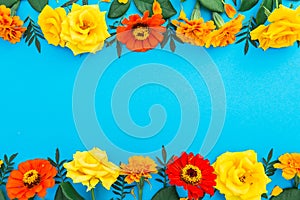 Floral border frame of yellow and red flowers on blue background. Flat lay, top view. Floral background.