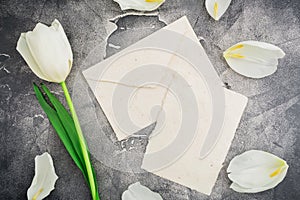 Floral composition with white tulips and paper envelope with card on dark background. Flat lay, top view. Floral pattern backgroun