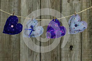 Floral fabric hearts hanging on clothesline by shabby wood background