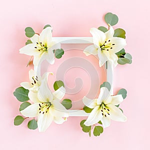 Floral frame made of white lilies and eucalyptus leaves on pink background. Flat lay, top view floral mockup with empty