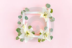 Floral frame made of white lilies and eucalyptus leaves on pink background. Flat lay, top view floral mockup with empty