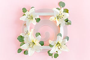 Floral frame made of white lilies and eucalyptus leaves on pink background. Flat lay, top view floral mockup with empty