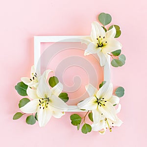 Floral frame made of white lilies and eucalyptus leaves on pink background. Flat lay, top view floral mockup with empty